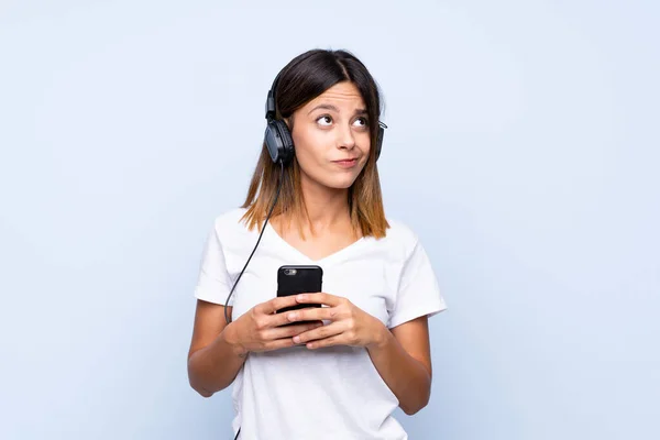 Jeune Femme Sur Fond Bleu Isolé Utilisant Mobile Avec Écouteurs — Photo