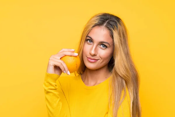 Junge Blonde Frau Hält Eine Orange Über Gelbem Hintergrund — Stockfoto