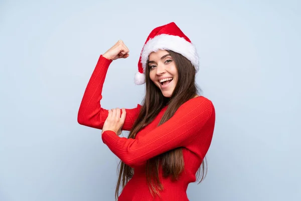 戴着圣诞礼帽的女孩在孤零零的蓝色背景下做着强有力的手势 — 图库照片