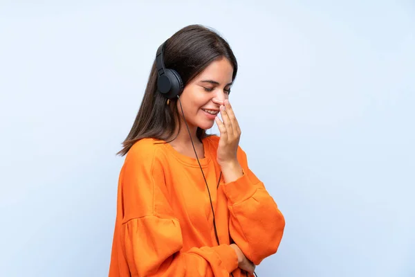 Young woman listening music with a mobile over isolated blue wall smiling a lot