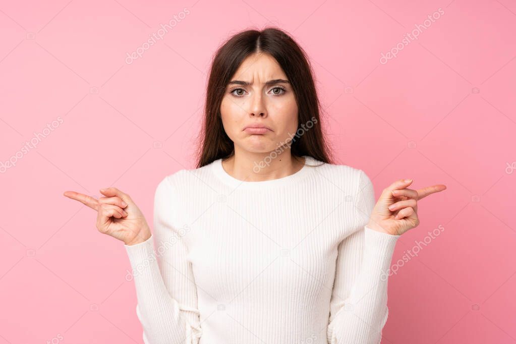 Young woman over isolated pink background pointing to the laterals having doubts