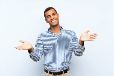 İzole edilmiş mavi arka planda genç, yakışıklı esmer adam sunar ve davet eder.