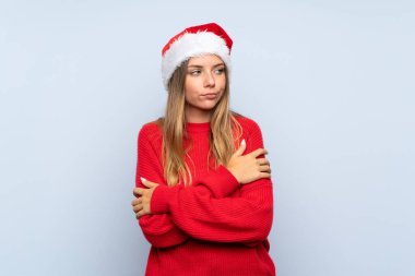 İzole edilmiş mavi arka plan üzerinde noel şapkası olan kız bir fikir düşünüyor.