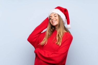 İzole edilmiş mavi arka planda, Noel şapkalı kız gülüyor.