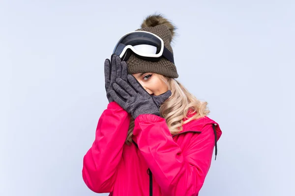 一个滑雪板的少女 戴着雪板眼镜 用蓝色的背景遮住眼睛 用手指看 — 图库照片