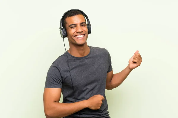 Genç yakışıklı adam izole yeşil duvar üzerinde bir cep ile müzik dinliyor — Stok fotoğraf