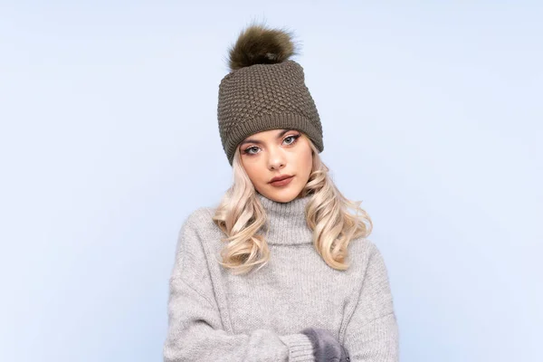 年轻少女 头戴冬帽 背负蓝色的孤立背景 双臂交叉 — 图库照片