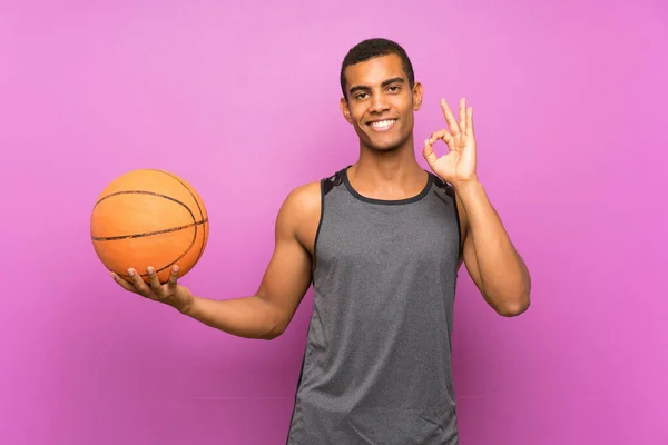Молодой Спортсмен Мячом Баскетбола Над Изолированной Фиолетовой Стеной Показывает Знак — стоковое фото