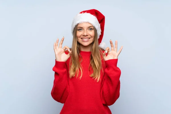 Дівчина Різдвяним Капелюхом Над Ізольованим Синім Тлом Показує Знак Пальцями — стокове фото