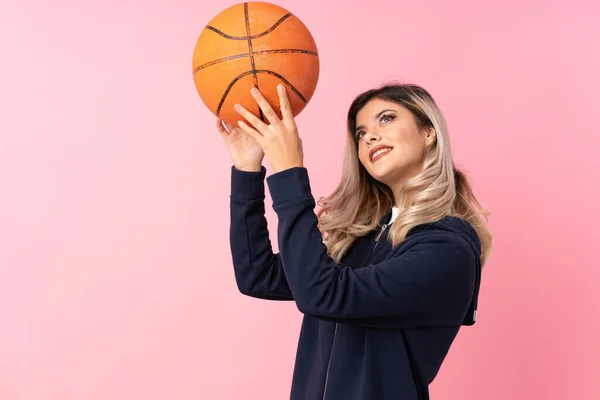 Teenager girl over isolated pink background with ball of basketball