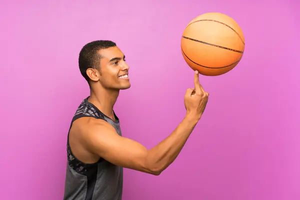 Молодой спортсмен с мячом баскетбола над изолированным фиолетовым валом — стоковое фото