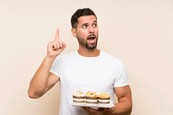 Handsome man holding muffin cake over isolated background intending to realizes the solution while lifting a finger up