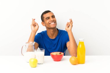 Genç adam kahvaltı yapıyor, parmakları çapraz.