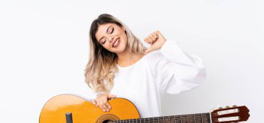 İzole edilmiş beyaz arka planda gitar çalan genç bir kız gururlu ve kendini beğenmiş.