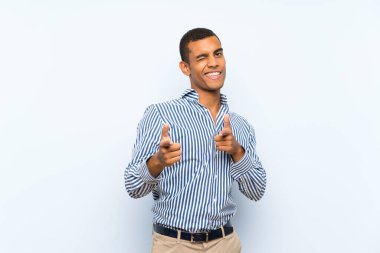 Genç, yakışıklı, esmer, soyutlanmış, mavi arka planda bir adam ön tarafı işaret ediyor ve gülümsüyor.