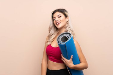 Genç bir spor kızı, izole edilmiş bir arka planda, bir paspas ve gülümsemeyle.