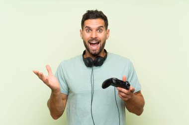 Genç yakışıklı bir adam video oyunu kontrolörüyle oynuyor. Yüzünde şok ifadesi olan yeşil bir duvarın üzerinde.
