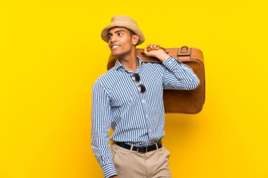 Esmer adam, izole edilmiş sarı arka planda antika bir evrak çantası tutuyor.