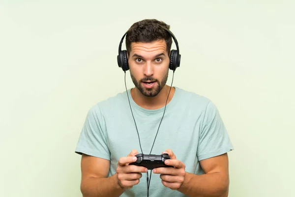 Young handsome man playing with a video game controller over isolated green wall — Stock Photo, Image