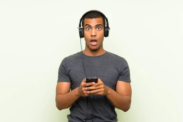 Joven hombre guapo escuchando música con un móvil sobre una pared verde aislada —  Fotos de Stock
