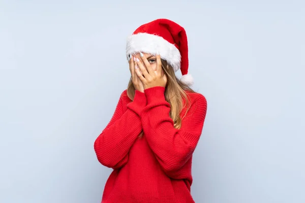 戴着圣诞帽的女孩 戴着一顶孤立的蓝色背景的帽子 蒙住眼睛 用手指看 — 图库照片