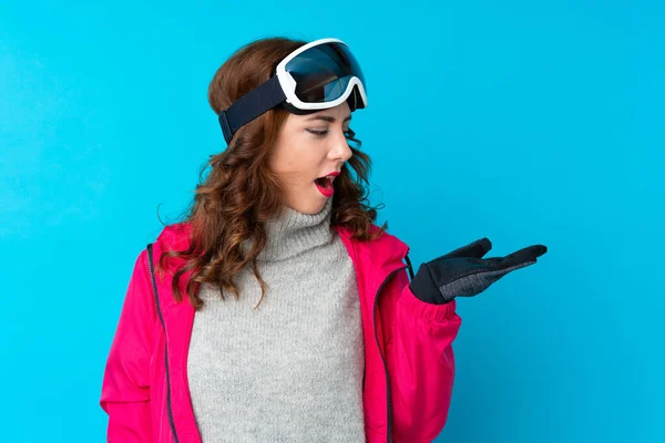 Narciarka Okularami Snowboardowymi Nad Odizolowaną Niebieską Ścianą Trzymająca Wyimaginowaną Przestrzeń — Zdjęcie stockowe