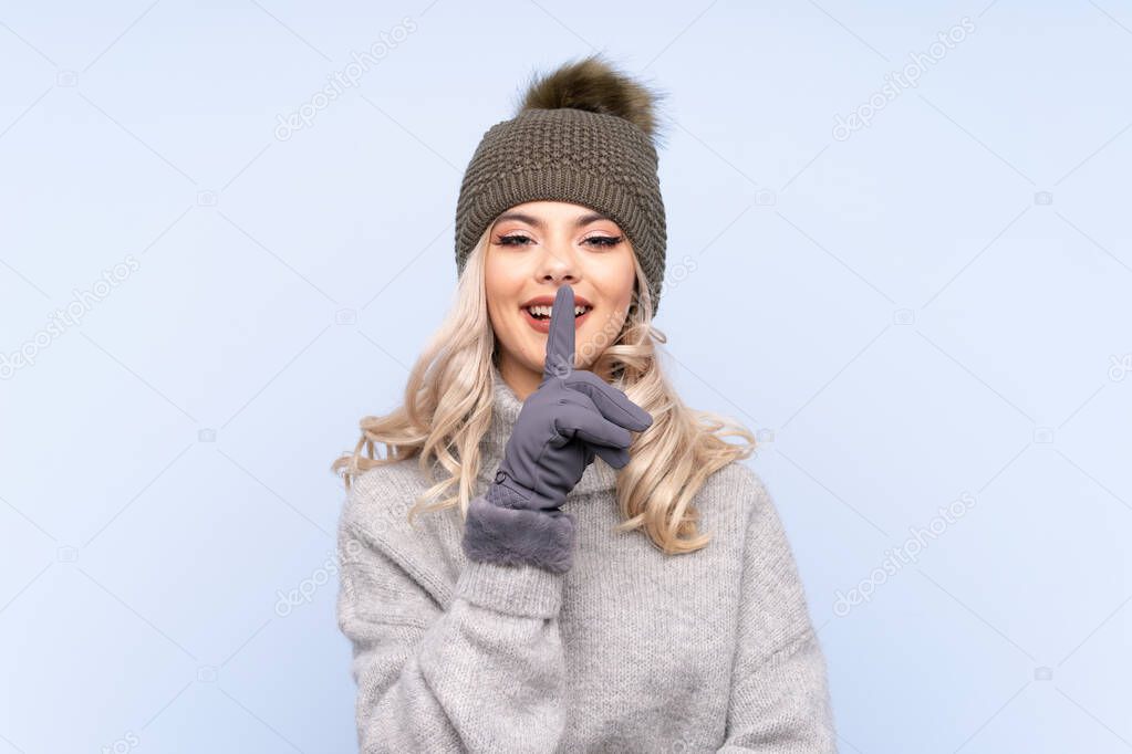 Young teenager girl with winter hat over isolated blue background doing silence gesture