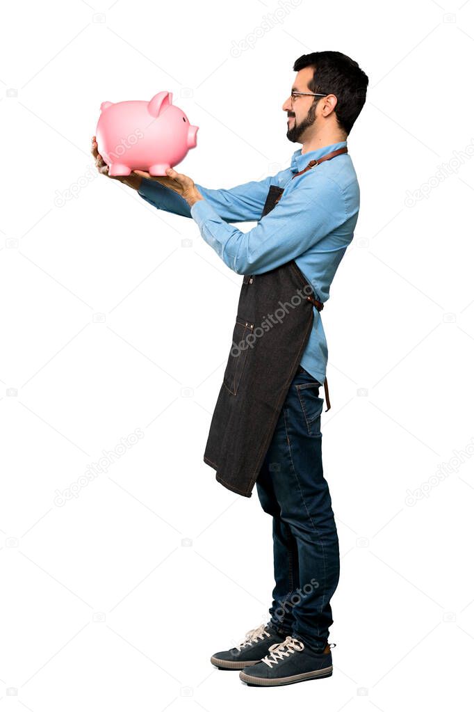 Full-length shot of Man with apron holding a piggybank over isolated white background