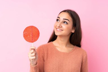 Pembe arka planda lolipop tutan genç kız gülümserken yukarı bakıyor.