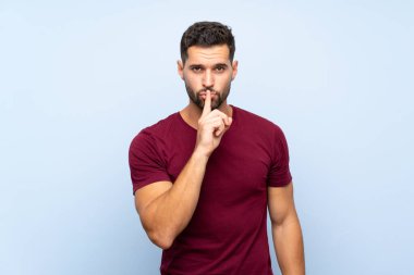 Izole mavi arka plan üzerinde yakışıklı adam ağzına parmak koyarak sessizlik jest bir işareti gösteren