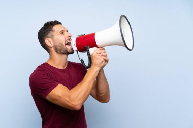 Izole mavi arka plan üzerinde yakışıklı adam bir megafon ile bağırıyor