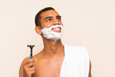 Genç yakışıklı adam, sakalını soyutlanmış arka planda tıraş edip gülümserken yukarı bakıyor.