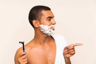 Genç ve yakışıklı bir adam sakalını sakalından ayırıp bir ürün sunmak için kenarı işaret ediyor.