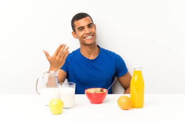 Genç adam kahvaltısını sofrada yapıyor. Gelmeye davet ediyor.