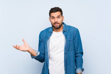İzole edilmiş mavi arka planda yakışıklı bir adam bir şeyi anlamadığı için mutsuz.