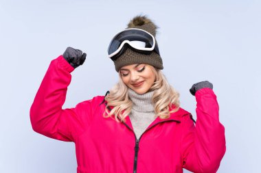 Kar kayağı gözlüklü genç kız izole edilmiş mavi arka planda zaferi kutluyor.