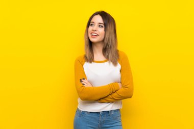 Güzel bir genç kadın, izole edilmiş sarı duvarda mutlu ve gülümsüyor.
