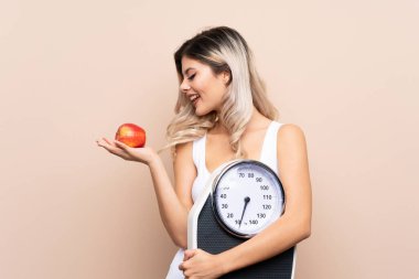 Tartı makinesi olan genç bir kız izole edilmiş arka planda elmaya bakarken bir tartı makinesi tutuyor.