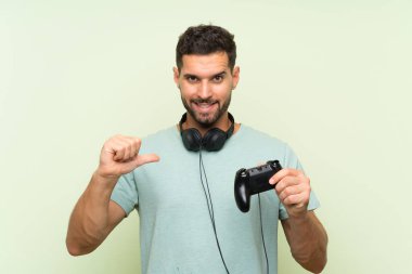 Genç yakışıklı bir adam, izole edilmiş yeşil duvarın üzerinde bilgisayar oyunu kontrolörüyle oynuyor gururlu ve kendinden memnun.