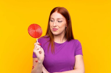 Sarı arka planda lolipop tutan genç kızıl saçlı kadın.
