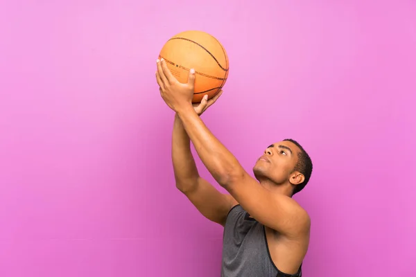 Pemuda olahraga dengan bola basket di atas dinding ungu terisolasi — Stok Foto