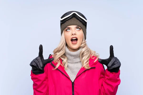一个滑雪板的少女 戴着雪板眼镜 带着蓝色的背景 用食指指尖着一个很好的主意 — 图库照片