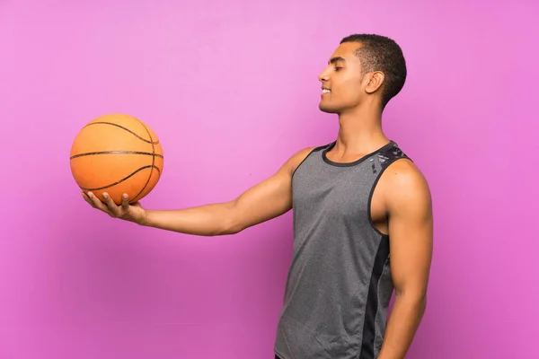 Young sport man with ball of basketball over isolated purple wall with happy expression