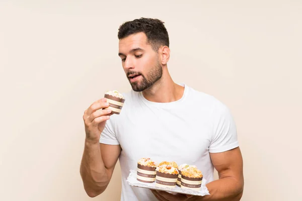 Hombre guapo sosteniendo pastel de magdalenas sobre fondo aislado — Foto de Stock