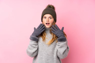 Kışlık şapkalı Ukraynalı genç kız izole pembe arka planda ve yüzünde sürpriz bir ifade var.
