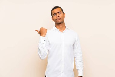 Genç yakışıklı esmer adam izole edilmiş arka planda mutsuz ve kenarı işaret ediyor.
