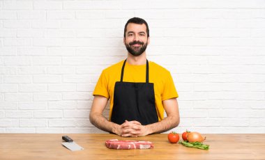 Aşçı mutfakta kolları kalçasında poz verip gülümsüyor.