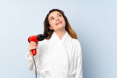 Saç kurutma makinesiyle bornozlu genç bir kadın gülümserken yukarı bakıyor.