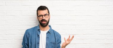 Beyaz tuğla duvarın üzerinde sakallı yakışıklı bir adam şüpheyle hareket ediyor.