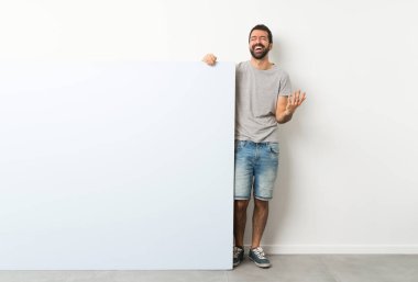 Sakallı genç yakışıklı adam elinde kocaman mavi bir pankartla gülümsüyor.